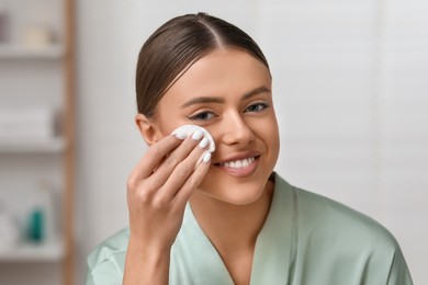 Beautiful woman removing makeup with cotton pad indoors