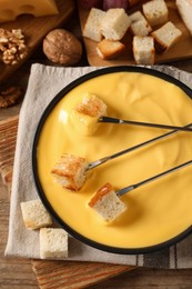 Tasty cheese fondue and forks with bread pieces on wooden table, flat lay