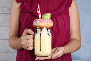 Photo of Woman with mason jar of delicious milk shake on light background, closeup