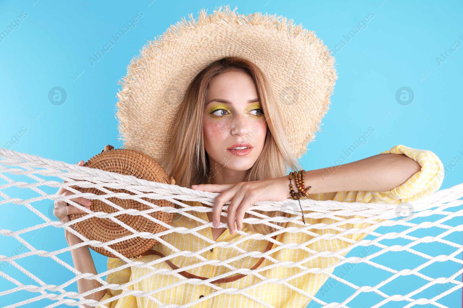 Photo of Beautiful young woman posing near net on color background. Summer fashion