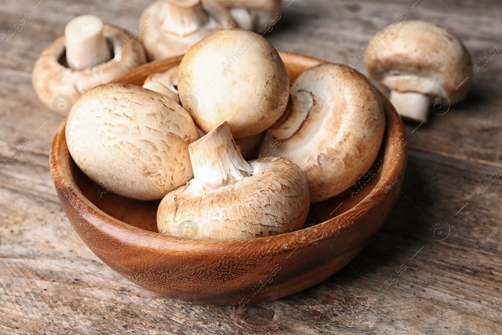 Photo of Bowl of fresh champignon mushrooms on wooden table, closeup