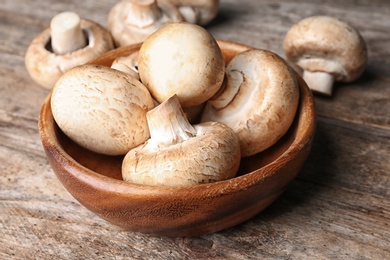 Photo of Bowl of fresh champignon mushrooms on wooden table, closeup
