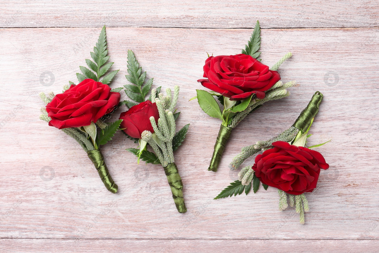 Photo of Many stylish red boutonnieres on light wooden table, flat lay