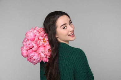 Photo of Beautiful young woman with bouquet of peonies on light grey background