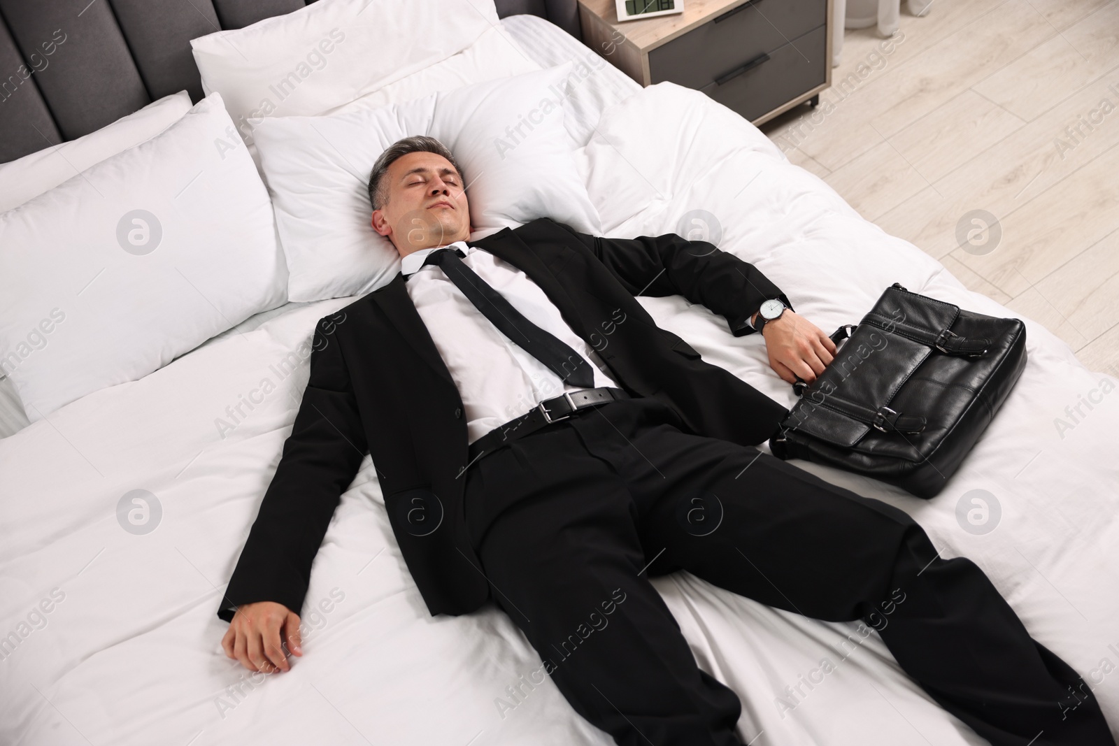 Photo of Businessman with briefcase sleeping on bed indoors