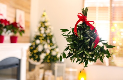 Photo of Mistletoe bunch with red bow hanging in room decorated for Christmas, space for text