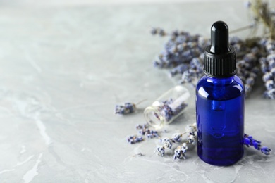 Bottle of natural essential oil and lavender flowers on grey marble background. Space for text