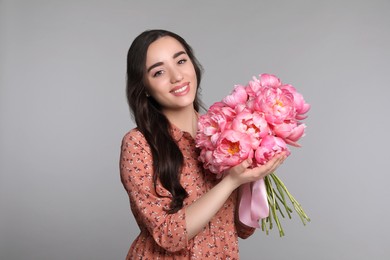 Beautiful young woman with bouquet of peonies on light grey background