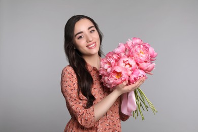 Photo of Beautiful young woman with bouquet of peonies on light grey background