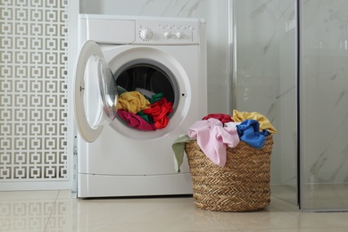 Photo of Wicker laundry basket with different clothes near washing machine in bathroom