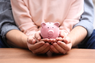 Photo of Couple with piggy bank at wooden table, closeup