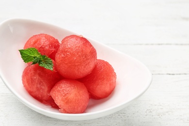 Plate of watermelon balls with mint on white wooden table, closeup