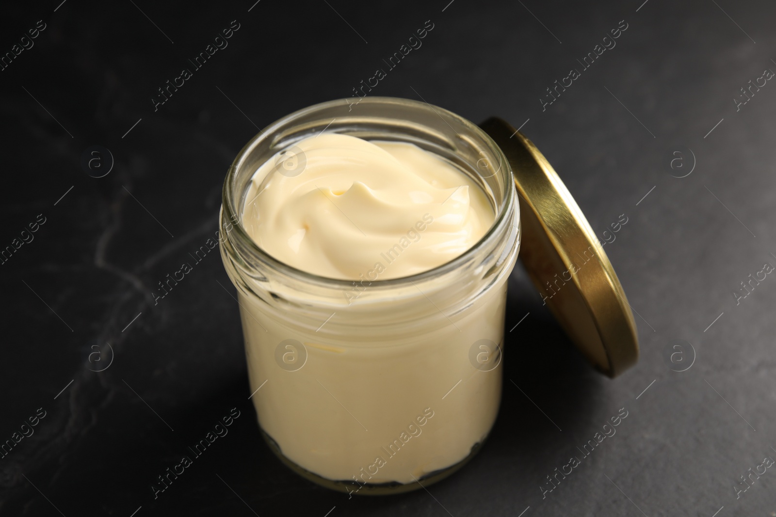 Photo of Jar of delicious mayonnaise and lid on black table