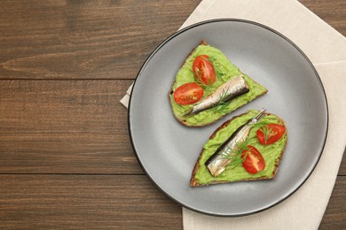 Photo of Delicious sandwiches with sprats, tomatoes, avocado puree and dill on wooden table, top view. Space for text
