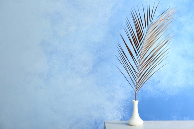 Photo of Vase with painted tropical Date palm leaf on table. Space for text