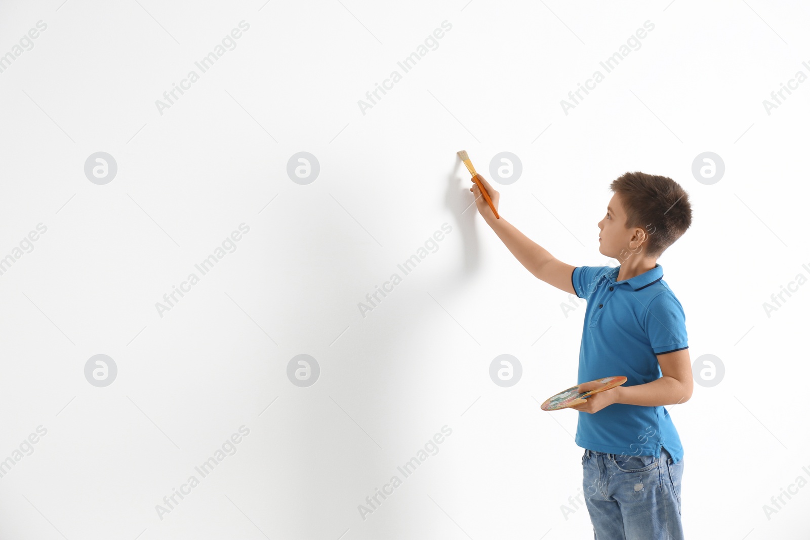 Photo of Little child painting on white wall indoors. Space for text