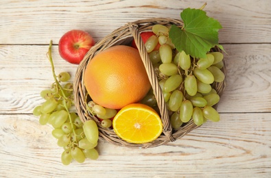 Photo of Wicker basket with different fruits on white wooden table, flat lay