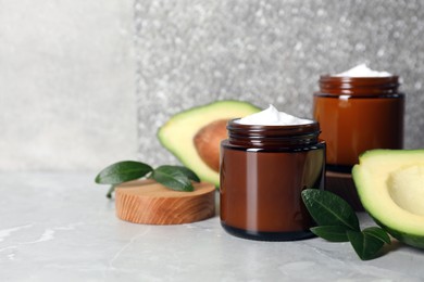 Photo of Jars of face cream and avocado on marble table. Space for text