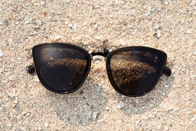 Stylish sunglasses on sandy beach, top view