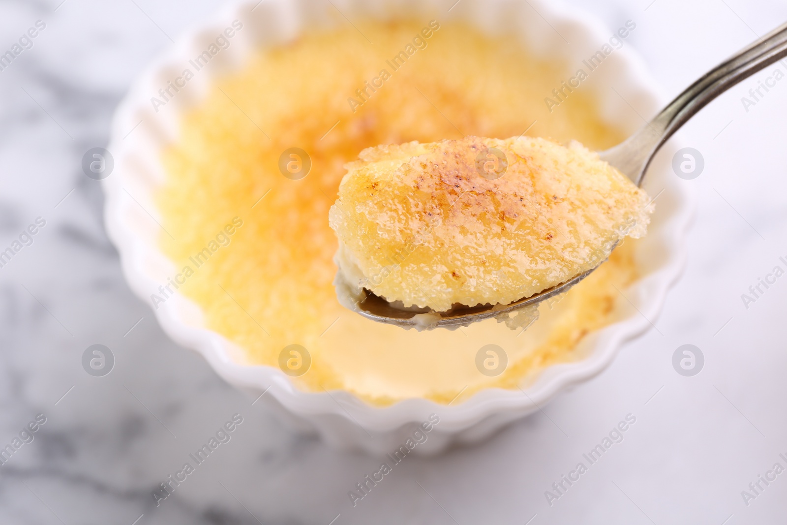 Photo of Eating delicious creme brulee at white marble table, closeup