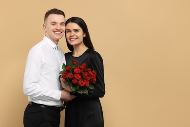 Photo of Lovely couple with bouquet of red roses on beige background, space for text. Valentine's day celebration
