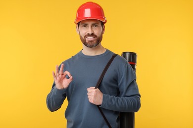 Photo of Architect in hard hat with drawing tube showing OK gesture on orange background