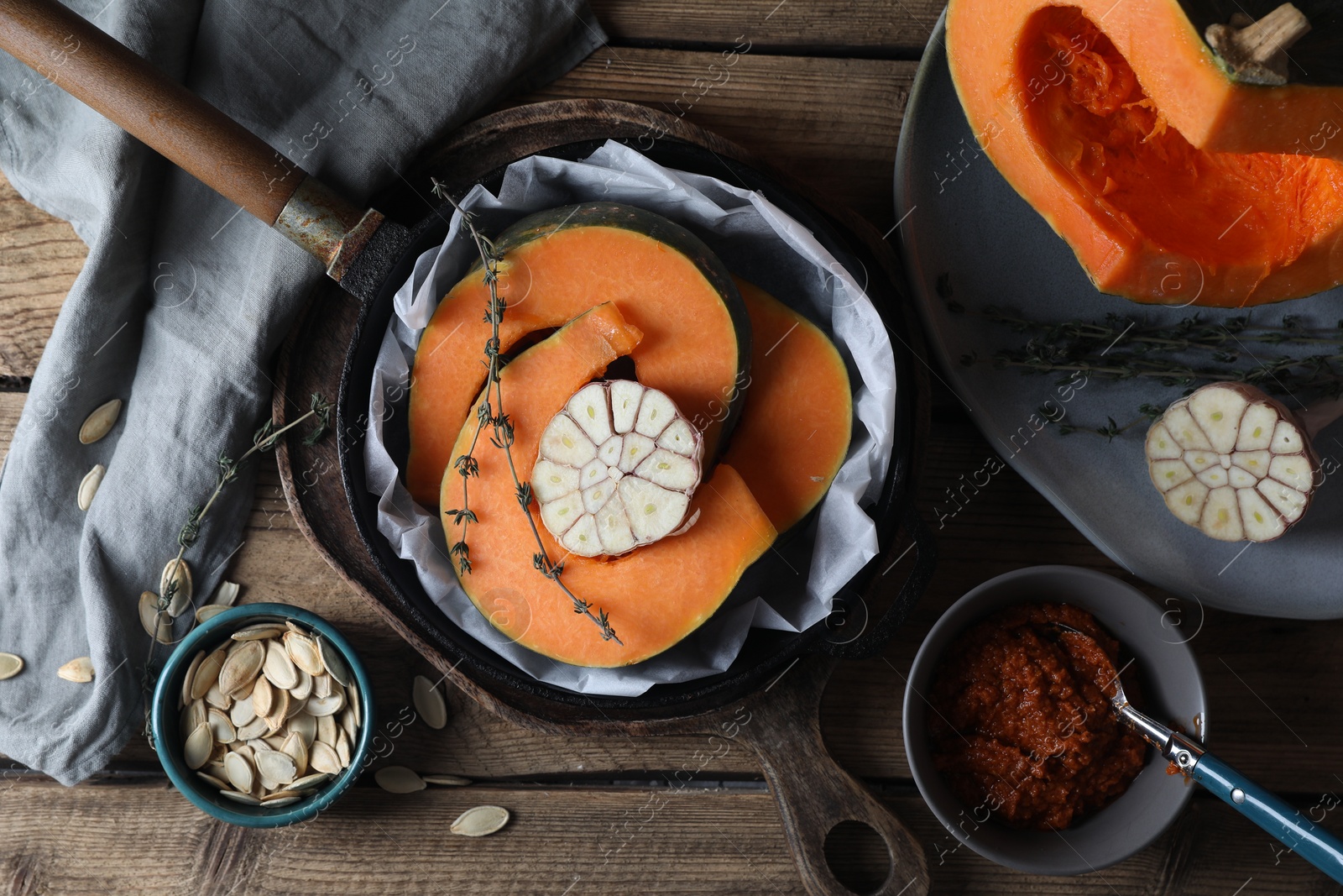 Photo of Fresh pumpkin slices with aromatic thyme and garlic in frying pan on wooden table, flat lay