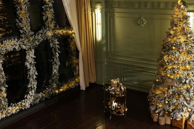 Photo of Beautiful decorated Christmas tree, table and festive decor near window indoors, space for text. Interior design