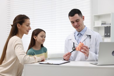 Gastroenterologist with model of stomach consulting woman and her daughter in clinic