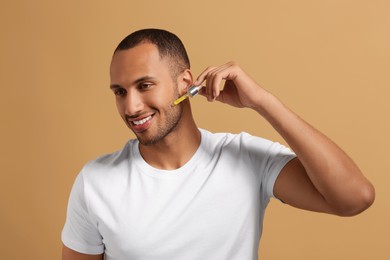 Handsome man applying cosmetic serum onto face on light brown background