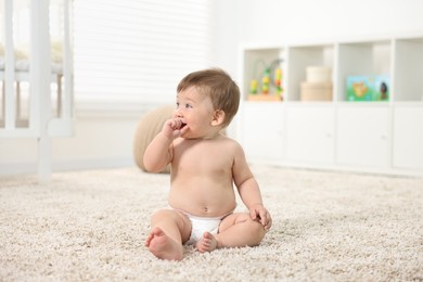 Cute baby boy sitting on carpet at home