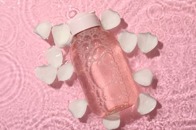 Photo of Wet bottle of micellar water and petals on pink background, top view