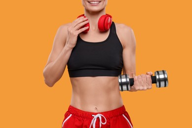 Photo of Sportswoman with dumbbell and headphones on yellow background, closeup