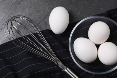 Photo of Metal whisk and raw eggs on dark grey table, flat lay