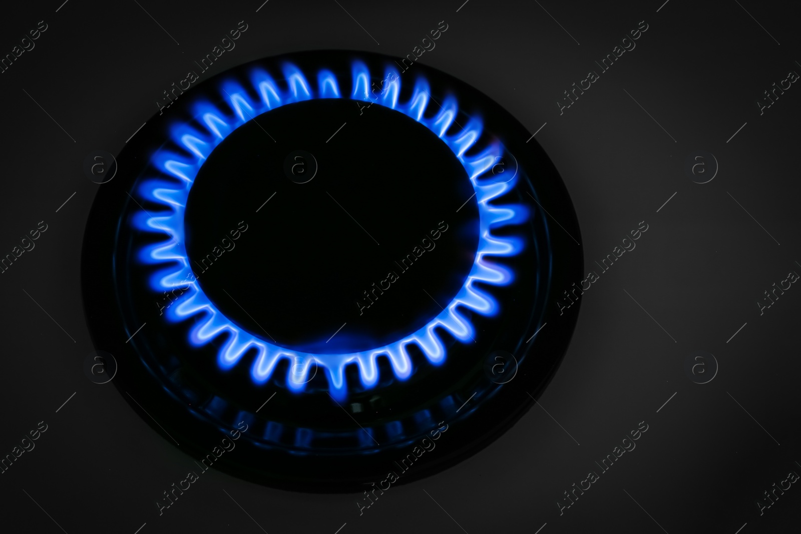 Photo of Gas burner of modern stove with burning blue flame at night, closeup