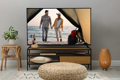 Image of Modern TV set on wooden stand in room. Scene of romantic movie on screen