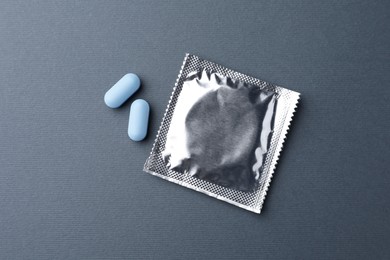 Photo of Pills and condom on dark gray background, flat lay. Potency problem