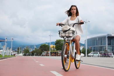 Photo of Beautiful young woman riding bicycle on lane in city. Space for text