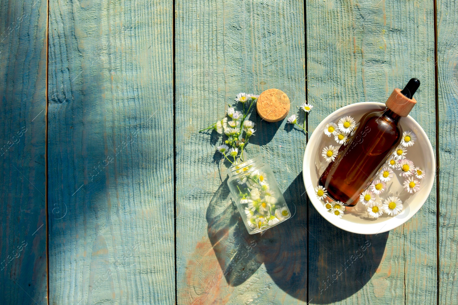 Photo of Bottle of chamomile essential oil and flowers on light blue wooden table, flat lay. Space for text