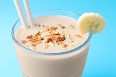 Photo of Glass of tasty banana smoothie with straws and nuts on light blue background, closeup