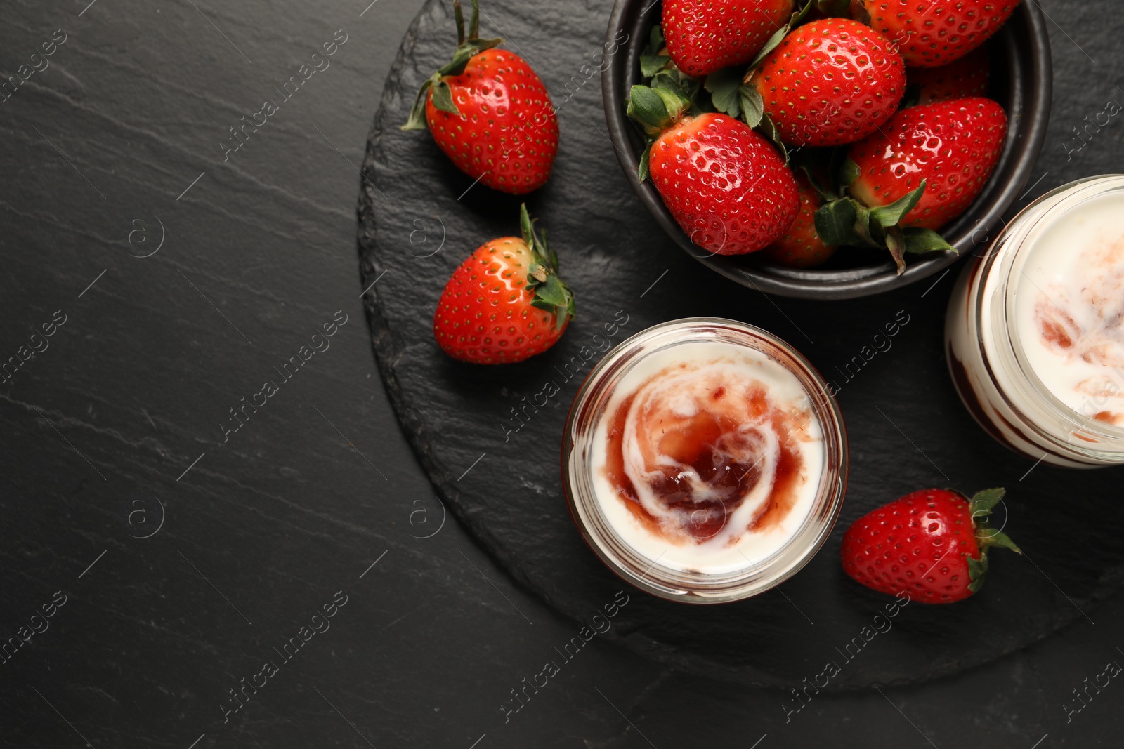 Photo of Tasty yoghurt with jam and strawberries on black table, top view. Space for text