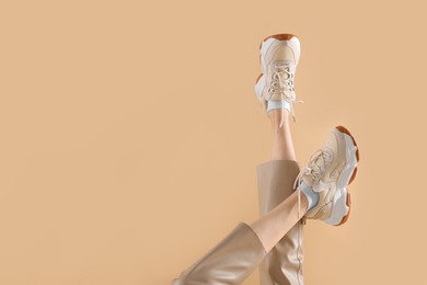 Woman wearing pair of new stylish sneakers on beige background, closeup. Space for text