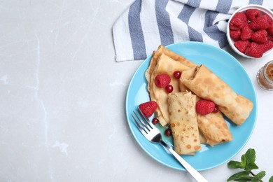 Photo of Delicious crepes served with berries and jam on light grey table, flat lay. Space for text