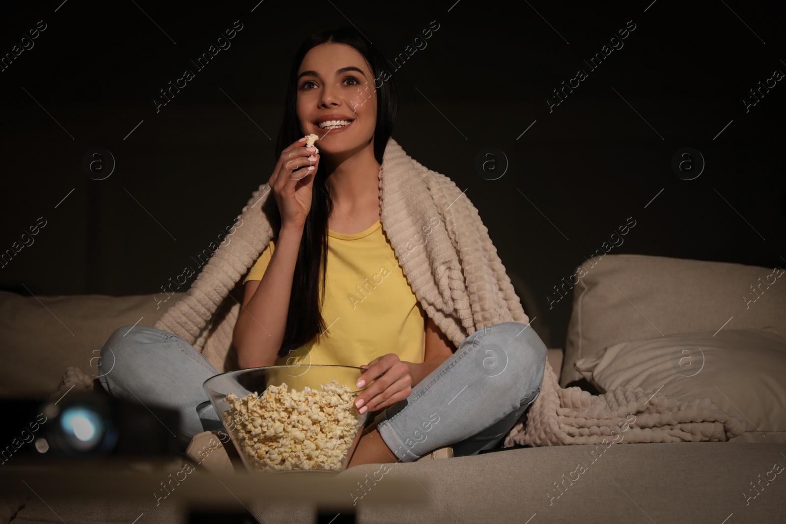 Photo of Young woman watching movie with popcorn on sofa at night