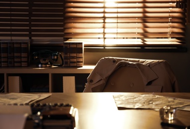 Grey coat on chair near wooden table in detective office