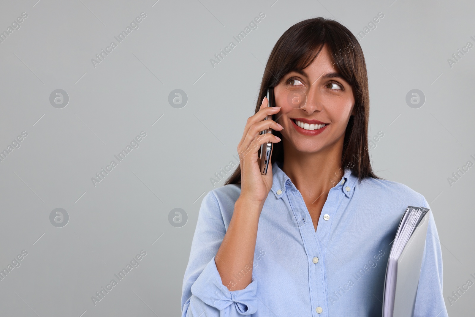 Photo of Happy secretary with folder talking on smartphone against light grey background. Space for text