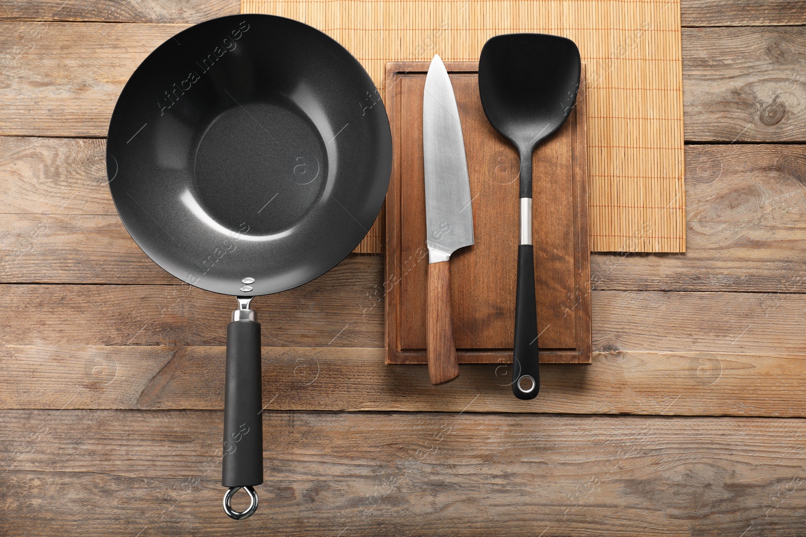 Photo of Black metal wok, knife and spatula on wooden table, top view