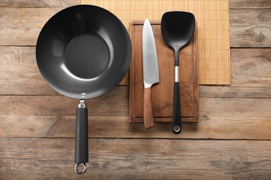 Black metal wok, knife and spatula on wooden table, top view