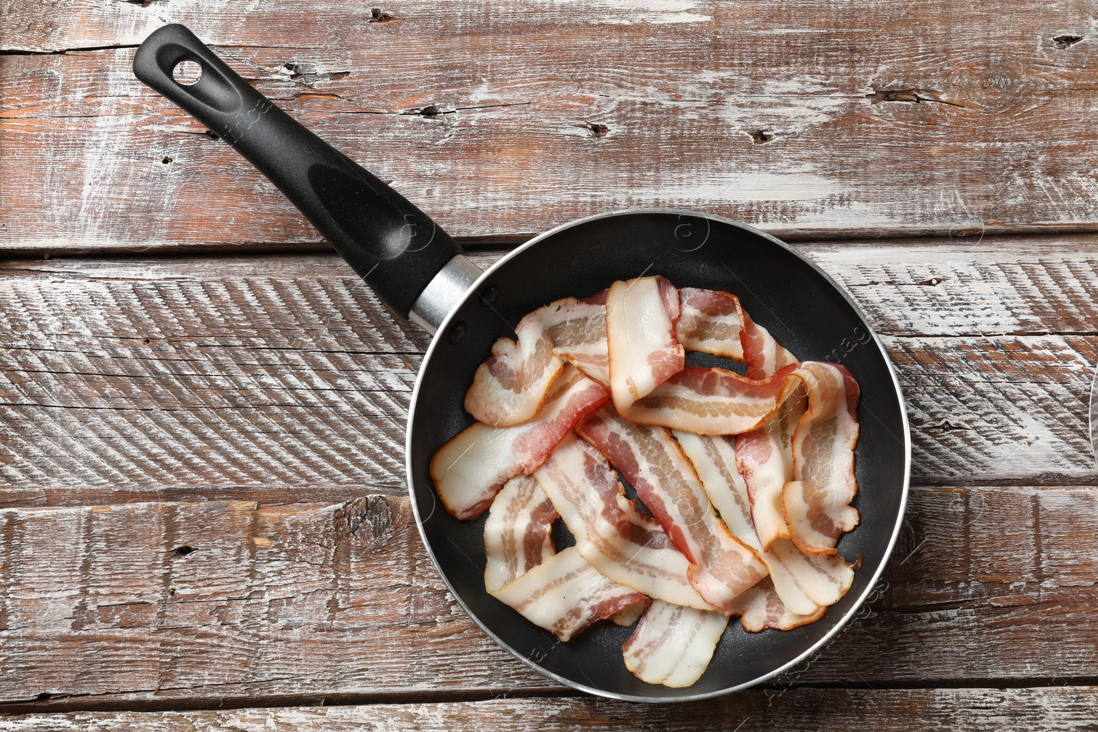 Photo of Delicious bacon slices in frying pan on wooden table, top view