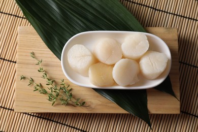 Fresh raw scallops, thyme and green leaves on bamboo mat, flat lay